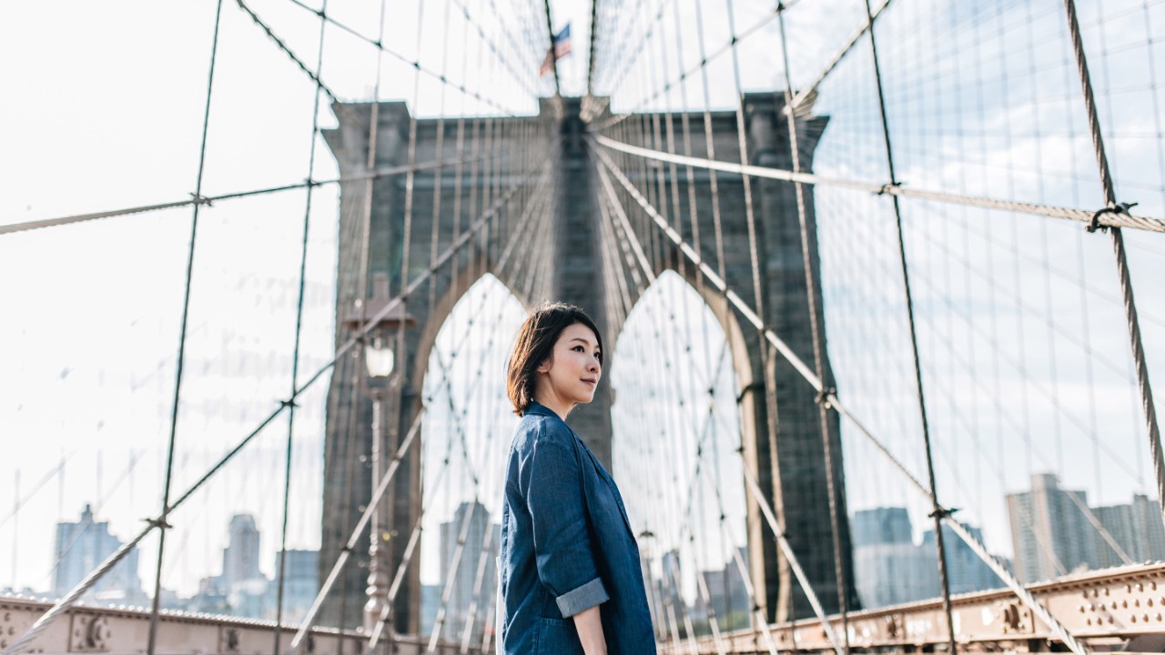 Young businesswoman looking up on Brooklyn Bridge against New York cityscape