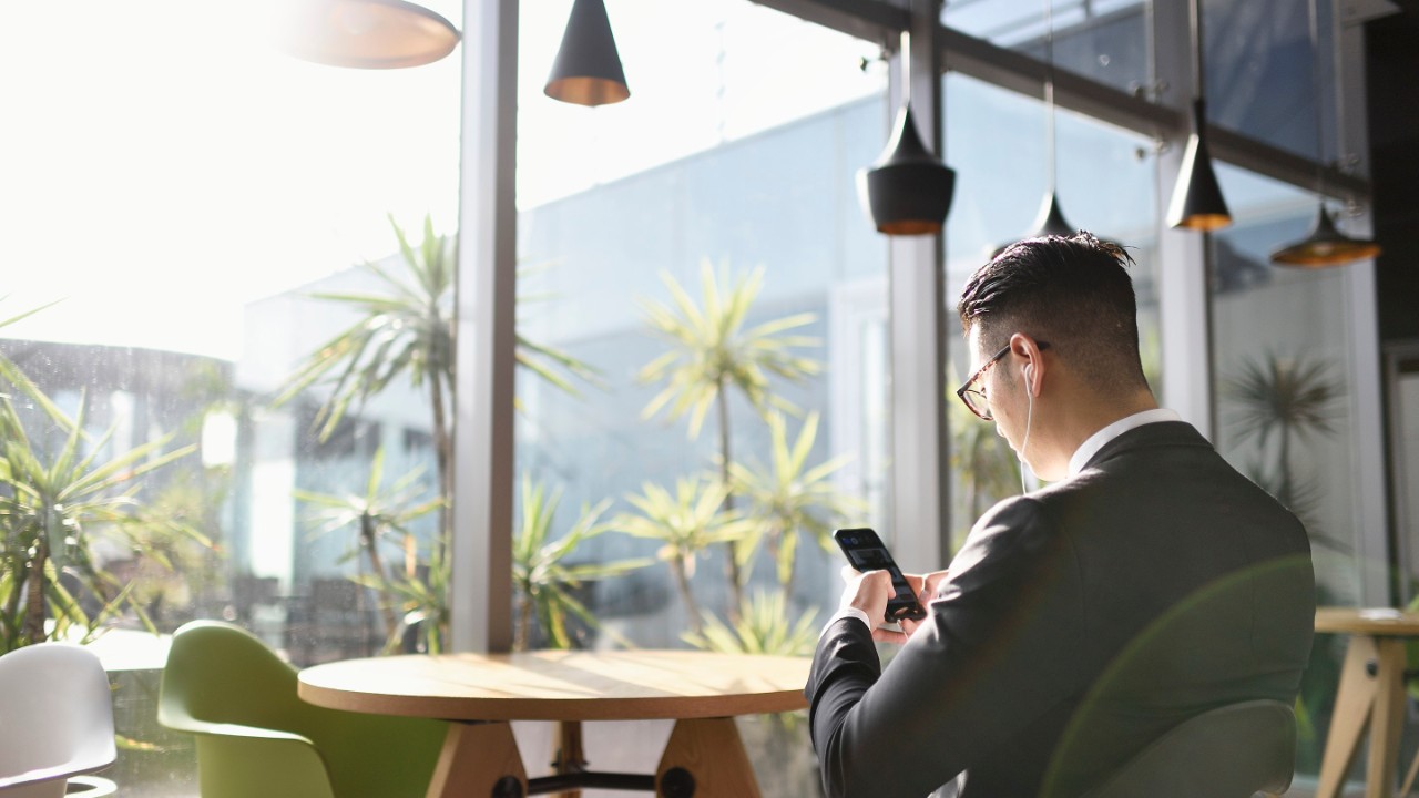 Mann i en dress som jobber fra telefonen sin, lytter til musikk med ørepropper