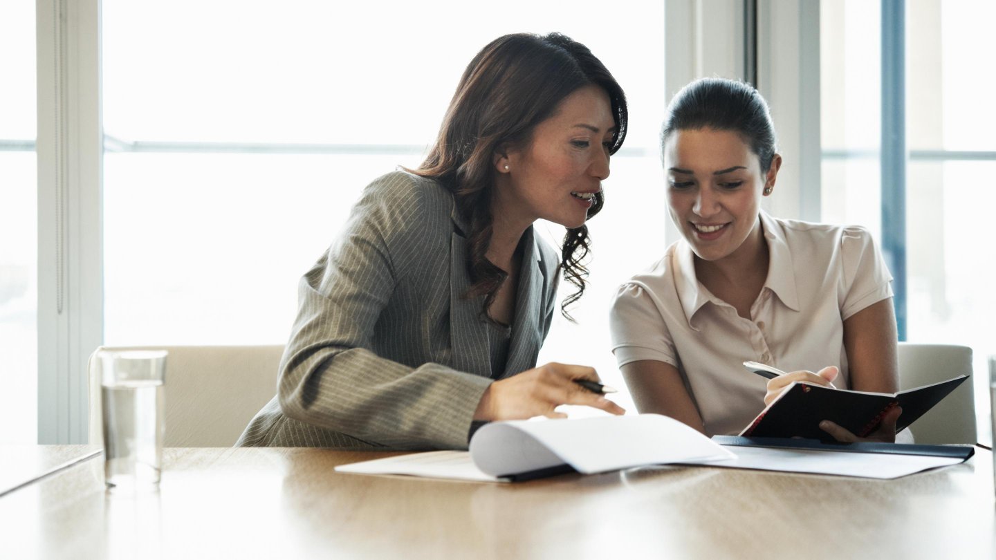Two office workers comparing notebooks.