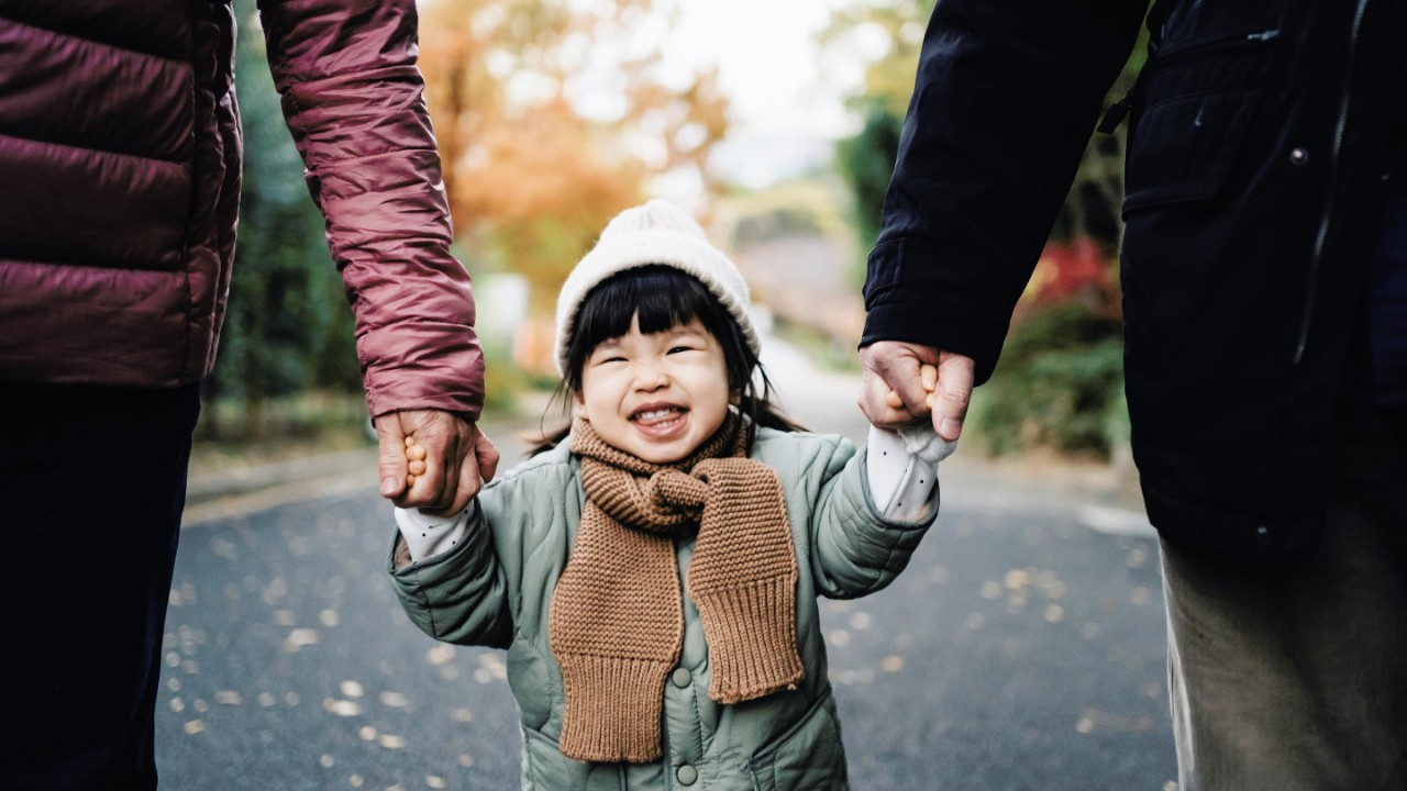 An asian girl holding adults hands.
