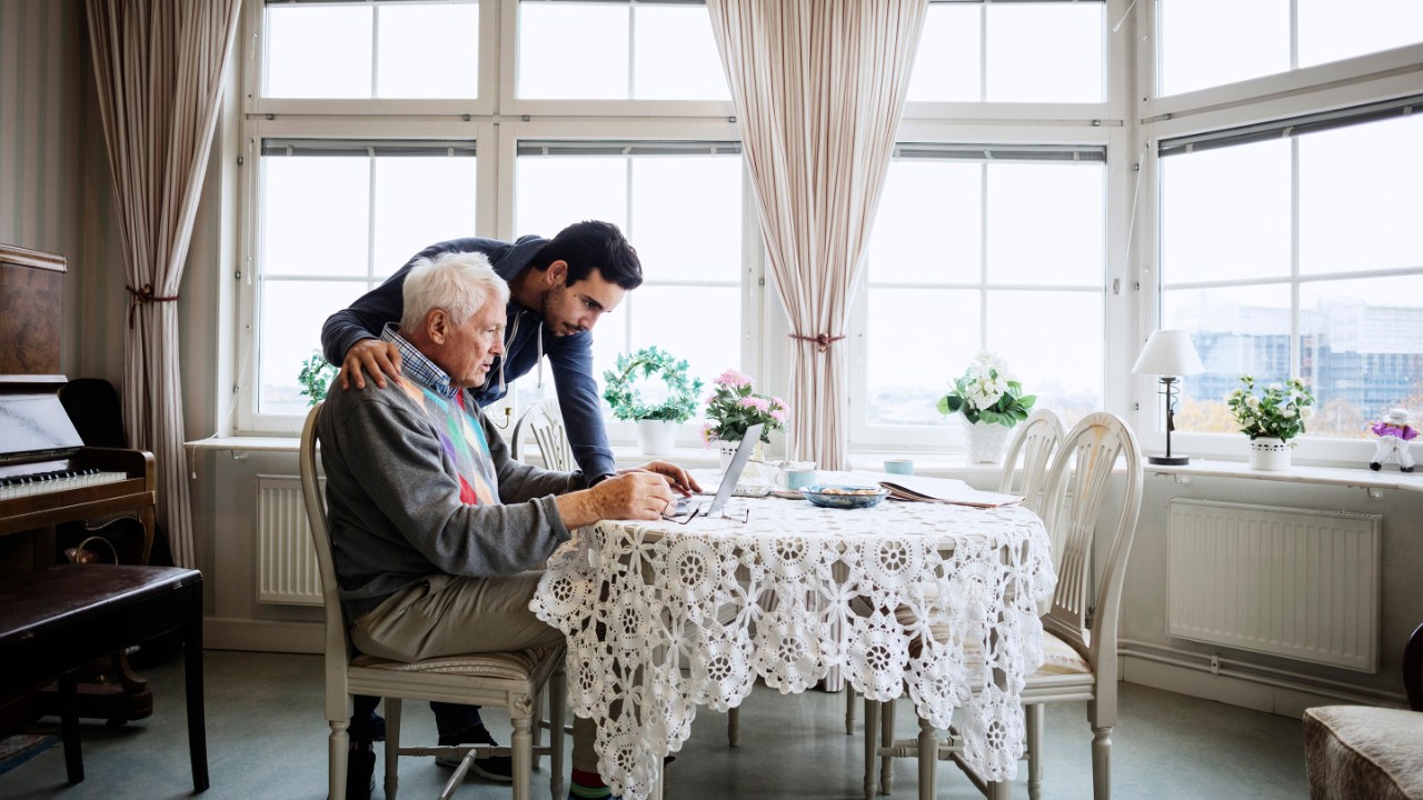 Senior man using laptop with caretaker at nursing home