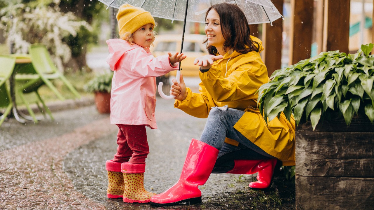 Mother with daughter walking in park in the rain wearing rubber boots