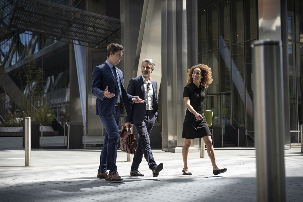 Three coworkers walking on city street with laptop discussing project