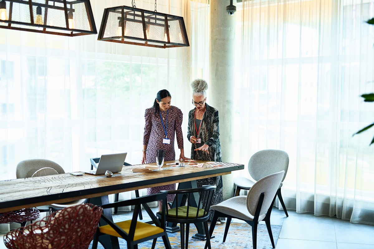 Two businesswomen standing by table and discussing ideas, collaboration, teamwork, creativity